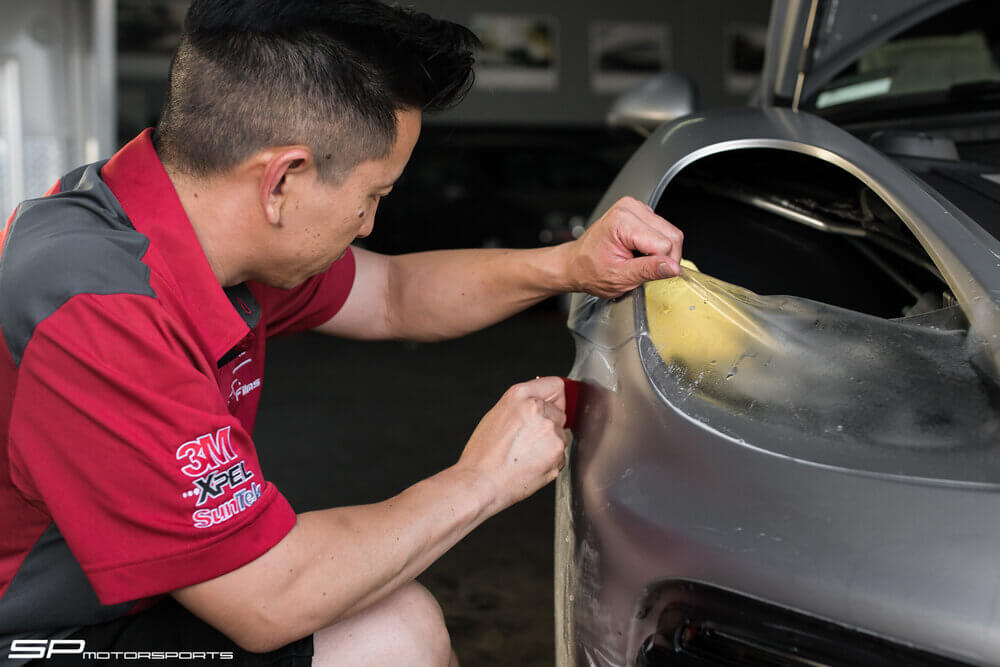 Custom Paint Protection Film – No pre-cuts here. To ensure the highest quality & results, all our PPF install is done by hand by our certified installers. We carry films by 3M, Xpel & SunTek, each with its unique design & optimized purpose. Our installers have the experience to custom tailor film for all makes & models, from Mclaren, Ferrari, BMW, Mercedes, Lamborghini & more. mechanic working underneath a lifted car